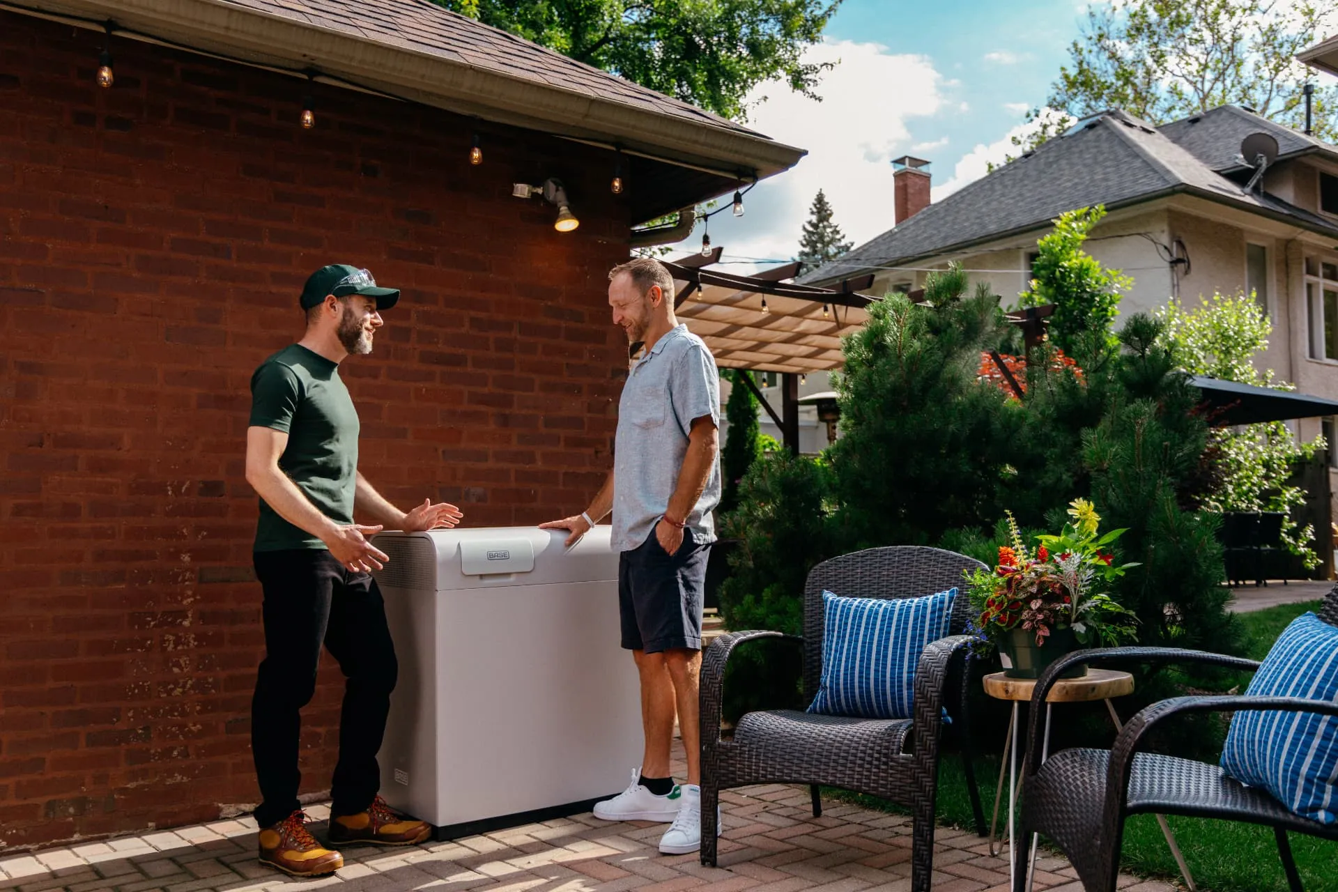 Base technician walking a homeowner through a newly installed home battery on a backyard patio