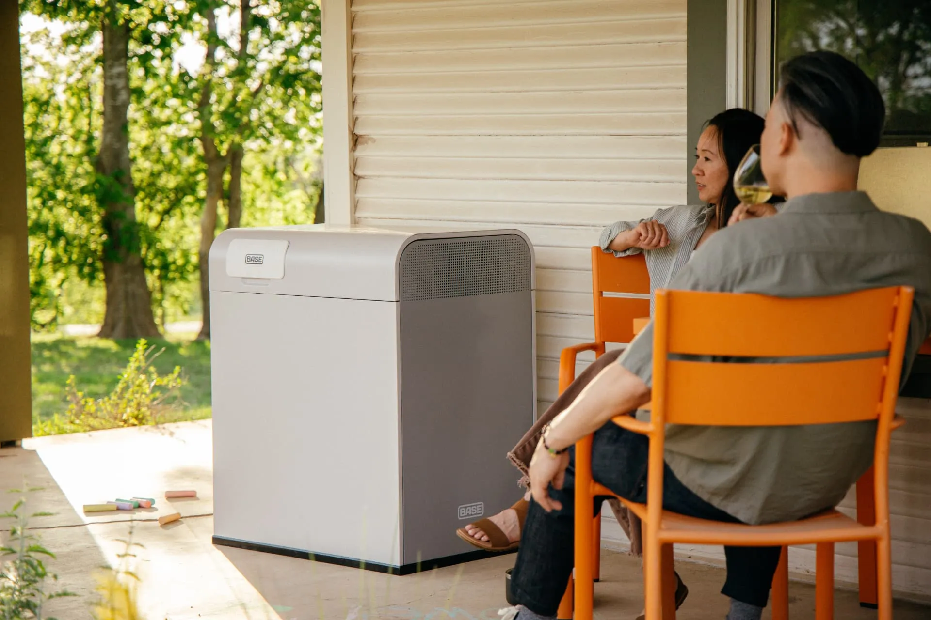 Couple relaxing on a porch beside a Base Power home battery