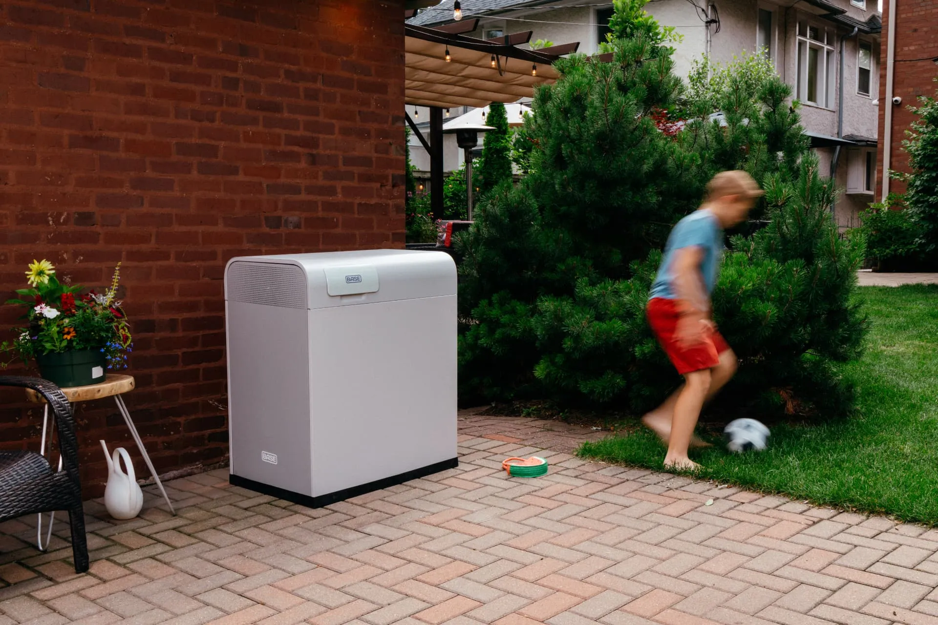 Boy kicking a soccer ball on a backyard patio near a Base Power battery