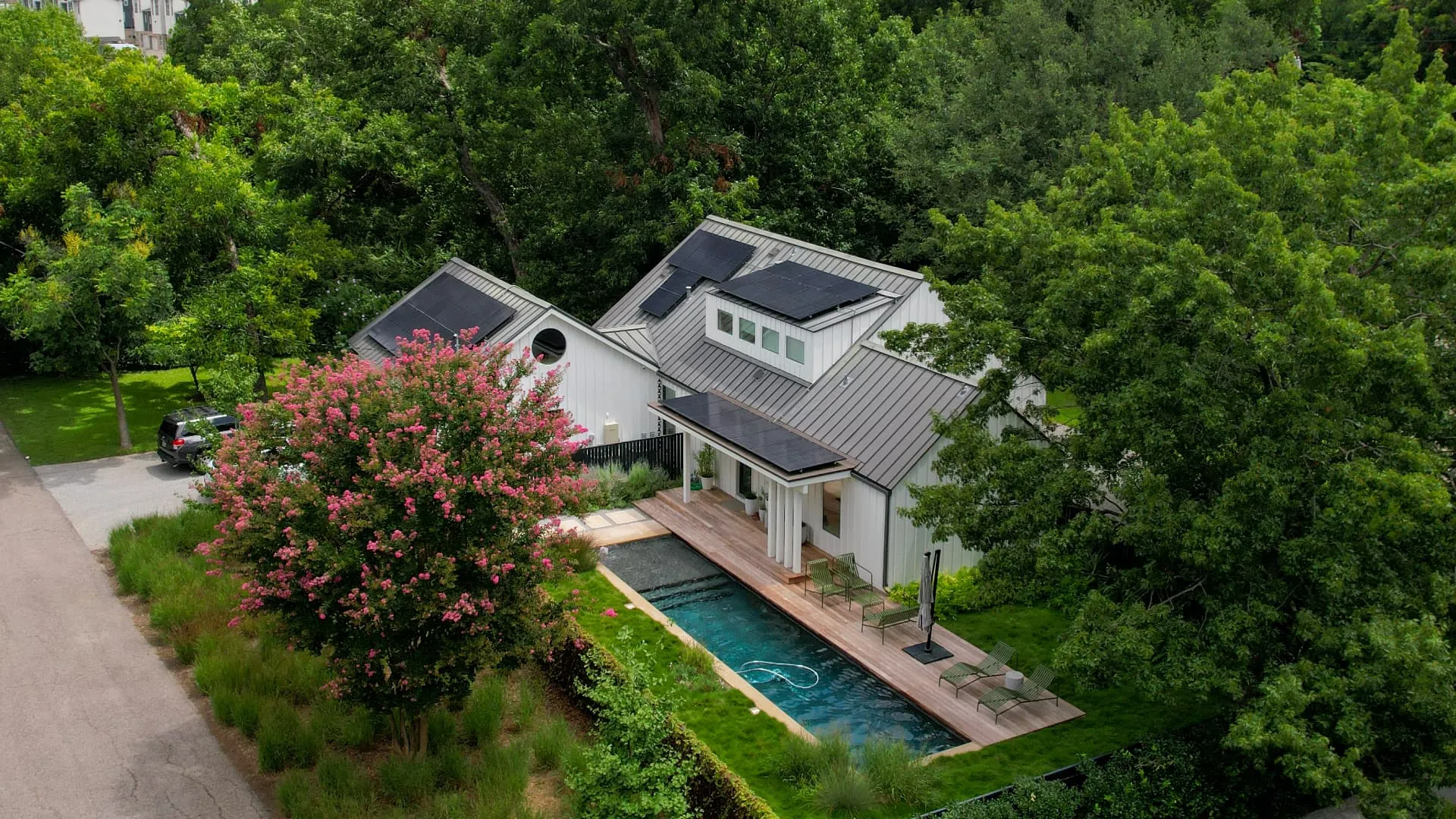 Aerial view of a Texas home with rooftop solar panels, a metal roof and a pool, surrounded by trees